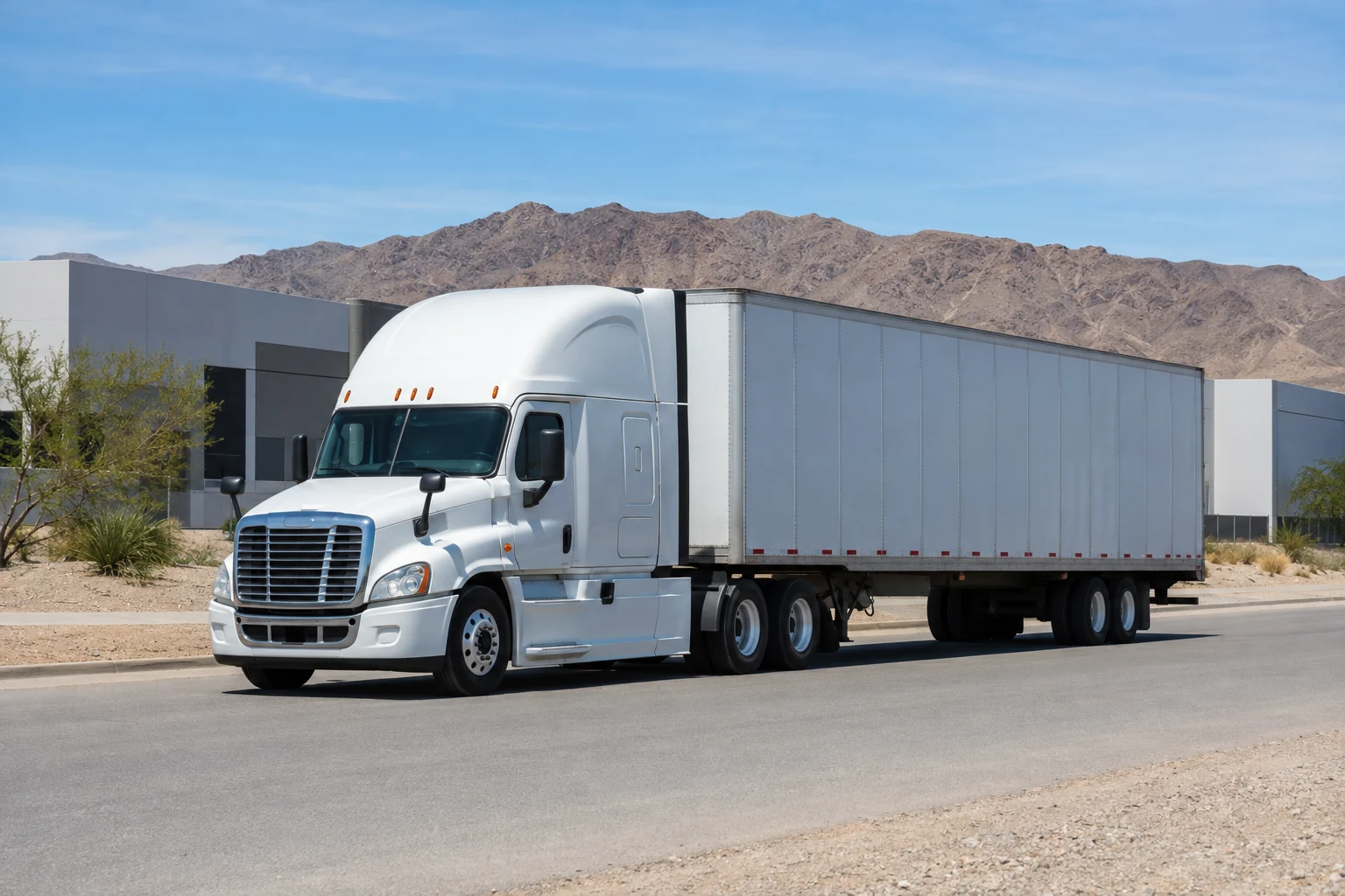 White tractor-trailer on a quiet industrial road with dry Nevada mountains behind it